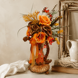 Bouquet vintage orange en fleurs de tissu monté sur un ancien chandelier en bois posé dans un atelier.