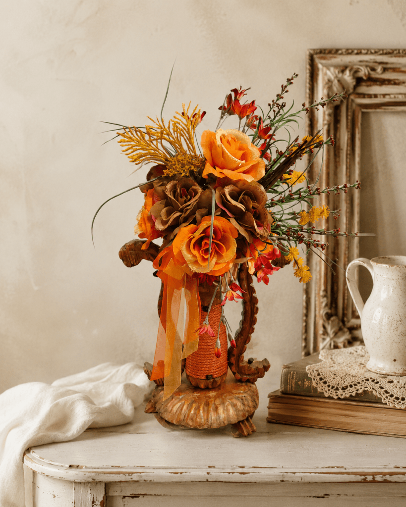 Bouquet vintage orange en fleurs de tissu monté sur un ancien chandelier en bois posé dans un atelier.